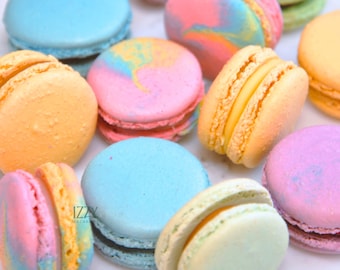 Puede incluir: Una colección de coloridos macarons en varios tonos pastel, incluyendo azul, rosa, amarillo y verde. Algunos macarons tienen un efecto veteado, mientras que otros son de colores sólidos. La imagen incluye el texto "Izzy Macarons".