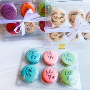 May include: Two clear plastic boxes filled with colorful macarons. The macarons are decorated with different designs and messages, including "Happy Birthday Alice", "Will you marry me?" and "Eat Me".