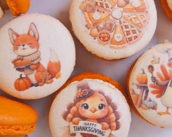 Könnte beinhalten: Nahaufnahme von mehreren dekorierten Macarons in Orange und Weiß. Die Macarons zeigen Thanksgiving-Motive, darunter einen Fuchs mit einem Kuchen, eine Truthahn mit einem Banner mit der Aufschrift "Happy Thanksgiving" und Kuchenstücke.