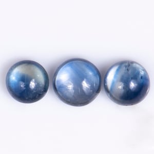 May include: Three round, cabochon-cut gemstones with a smooth, polished surface. The stones display a gradient of deep blue to translucent white, featuring internal inclusions and light reflections across their curved, dome-shaped tops.