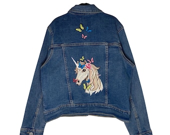 May include: A blue denim jacket with an embroidered unicorn with a rainbow mane and flowers on its head. The unicorn is surrounded by colorful butterflies.