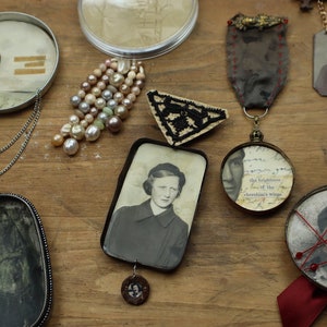Op de afbeelding: Een assortiment vintage sieraden en aandenkens, waaronder een parelketting, ingelijste foto's en decoratieve hangers. De items zijn gerangschikt op een houten oppervlak, wat een nostalgische en artistieke weergave creëert.