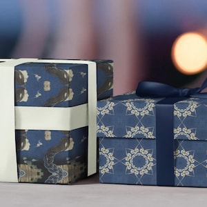 May include: Two rectangular gift boxes wrapped in patterned paper. The left box features a dark blue paper with a repeating abstract design and a wide white ribbon. The right box features a blue paper with a geometric floral pattern and a dark blue ribbon.