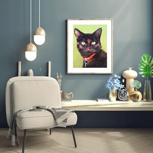 Pu&ograve; includere: Una stampa incorniciata con un gatto nero con gli occhi verdi e un collare rosso. Il gatto guarda direttamente lo spettatore. La stampa &egrave; appesa a un muro blu sopra una sedia bianca.