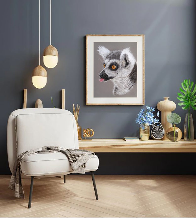 May include: A white armchair with a black throw and a wooden frame sits in a room with a grey wall. A framed print of a lemur with a long tongue hanging out is on the wall. There are two pendant lights hanging from the ceiling.
