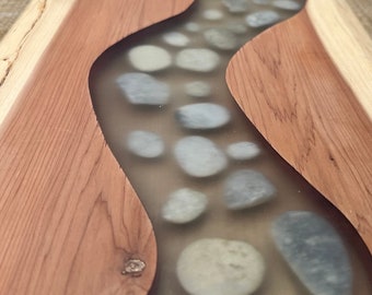 May include: A wooden serving tray with a clear epoxy river design. The river is filled with small, white and gray stones.