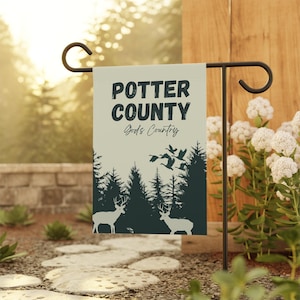 May include: A garden flag with the text "POTTER COUNTY God's Country" in black. The flag features a forest scene with deer and flying birds in a dark green color. The flag is displayed on a black metal stand.