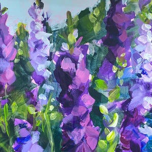 Op de afbeelding: Origineel schilderij van paarse en lavendelkleurige bloemen met groene bladeren. Het kunstwerk is ingelijst in een goudkleurige lijst. De penseelstreken zijn zichtbaar, waardoor een textuureffect ontstaat. De achtergrond is lichtblauw.