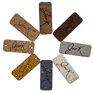 May include: Eight rectangular cork tags with the word "JessK" written in black ink.  Some tags have a brown, tan, or grey background.  One tag has the text "JessK.ca" printed on it.