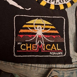 May include: Embroidered patch featuring a spider design against a sunset backdrop in yellow, orange, and red. The text "MY CHEMICAL ROMANCE" is embroidered below the design. The patch is bordered with a white stitch.