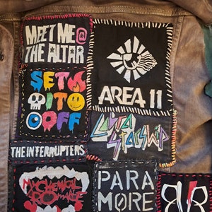 Könnte beinhalten: Braune Jeansjacke mit mehreren Aufnähern mit Bandnamen und Logos. Zu den Aufnähern gehören "MEET ME @ THE ALTAR", "AREA 11", "SET IT OFF", "THE INTERRUPTERS", "MY CHEMICAL ROMANCE", "LYRA STARSHIP", "PARAMORE" und ein stilisiertes Logo.