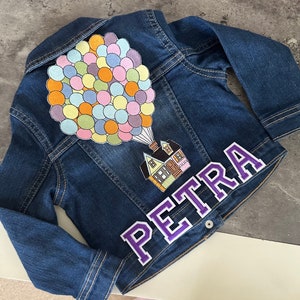 May include: A blue denim jacket with an embroidered patch of a house with balloons and the name "PETRA" in purple lettering.