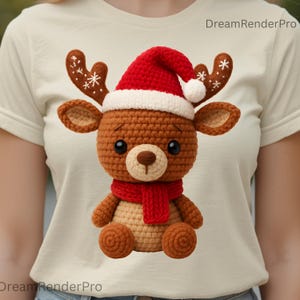 Peut inclure: Un renne au crochet portant un bonnet de Père Noël rouge, une écharpe et des bois avec des accents de flocons de neige. Le renne a de grands yeux noirs et est assis. Le renne est marron, beige et rouge. L'image est sur un t-shirt crème.
