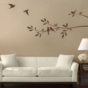 May include: A brown wall decal featuring a tree branch with leaves and four birds. The decal is applied to a wall above a white sofa.
