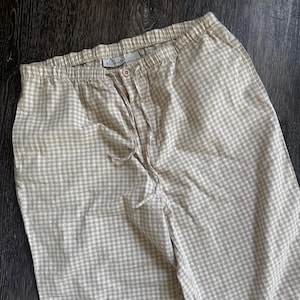 May include: Cream and white checked pajama trousers with an elasticated waistband and drawstring. The trousers have a button fastening and a relaxed fit. The fabric appears lightweight, suitable for sleepwear or lounging.