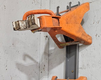May include: Two orange metal jack stands mounted on a wall. Each stand has a curved handle and a white and brown support. The stands are attached to a gray metal bar.