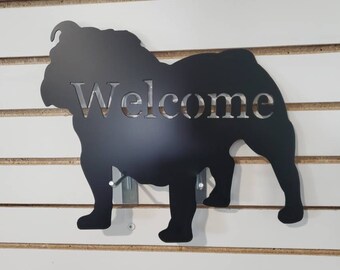 May include: Black metal silhouette of a bulldog with the word "Welcome" cut out of the silhouette. The silhouette is mounted on a white wall.