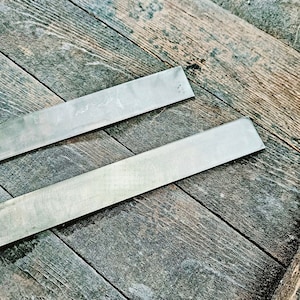 May include: Two long, thin, silver metal strips on a dark brown wooden surface.