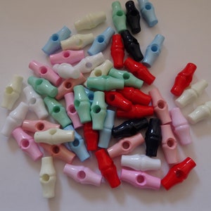 May include: A selection of colourful plastic toggle clasps in shades of pink, blue, green, red, black, and white. Each clasp has a cylindrical form with a central hole for threading. These clasps are likely used for jewellery making or crafting.