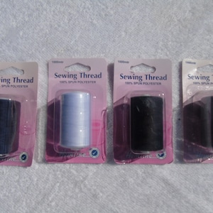 May include: Four spools of sewing thread in navy, light blue, black, and grey. Each spool is packaged in a clear plastic blister pack with a pink backing. The packaging reads "Sewing Thread 100% SPUN POLYESTER".