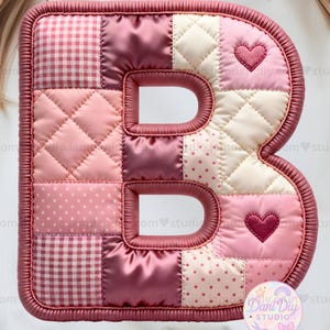 Puede incluir: Una letra "B" acolchada en tonos rosa, crema y burdeos. La letra presenta un diseño de patchwork con varios patrones, incluyendo cuadros, lunares y secciones acolchadas. Se ven dos acentos en forma de corazón. El borde es de un rosa más oscuro.