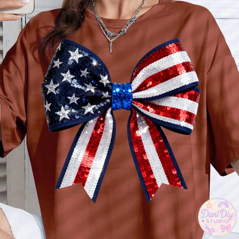 Peut inclure: Un t-shirt marron orn&eacute; d'un grand n&oelig;ud orn&eacute; de paillettes aux couleurs patriotiques. Le n&oelig;ud reprend le drapeau am&eacute;ricain avec des paillettes bleues, blanches et rouges. Le n&oelig;ud est centr&eacute; sur le t-shirt, cr&eacute;ant un look festif et accrocheur.
