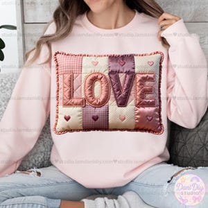 May include: A light pink sweatshirt featuring a patchwork design with the word "LOVE" in large, textured letters. The patchwork includes various patterns and colors, with heart accents. The sweatshirt is a comfortable, casual style.