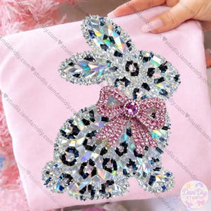 May include: A bedazzled bunny design with a pink bow and a leopard print pattern. The bunny is made of sparkling crystals and is set against a pink background. The image includes the text "Dani Diy Studio".