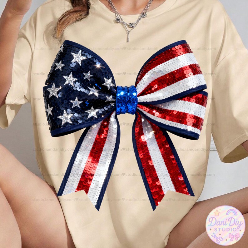Peut inclure: Un t-shirt beige orn&eacute; d'un grand n&oelig;ud &agrave; paillettes aux couleurs du drapeau am&eacute;ricain. Le n&oelig;ud pr&eacute;sente une section bleue avec des &eacute;toiles argent&eacute;es et des rayures rouges et blanches. Le n&oelig;ud est centr&eacute; sur le t-shirt.