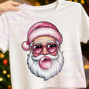 Puede incluir: Camiseta blanca con un diseño de Papá Noel. Papá Noel lleva un gorro rosa y gafas de sol en forma de corazón, soplando una burbuja de chicle. Un diseño divertido y festivo para la temporada navideña.