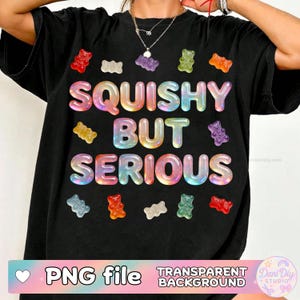 Puede incluir: Camiseta negra con la frase "SQUISHY BUT SERIOUS" en letras de burbujas arcoíris, rodeada de gráficos de ositos de goma coloridos. La parte inferior de la camiseta tiene una pancarta rosa con el texto "PNG file" y "TRANSPARENT BACKGROUND".