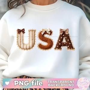 Puede incluir: Sudadera blanca con la palabra "USA" en letras decorativas. La "U" es a rayas, la "S" es de punto y la "A" es marrón con estrellas blancas. Cada letra tiene un lazo y un ribete de encaje.