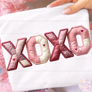 Puede incluir: Tela blanca con las letras "XOXO" aplicadas en un estilo patchwork. Las letras son en tonos rosa y rojo, con acentos de corazón. Las letras están delineadas con una costura roja más oscura.
