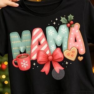Puede incluir: Camiseta negra con la palabra "MAMA" en un diseño festivo. Las letras están adornadas con motivos navideños como copos de nieve, acebo, un lazo rojo y galletas de jengibre. También se incluye una taza roja con un copo de nieve.