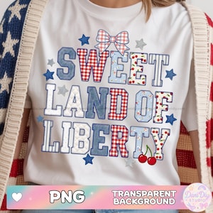 Puede incluir: Camiseta blanca con el texto "SWEET LAND OF LIBERTY" en un diseño de patchwork. Las letras presentan cuadros rojos, mezclilla azul y patrones florales. Los acentos incluyen estrellas, un lazo y cerezas. La camiseta es de temática patriótica.
