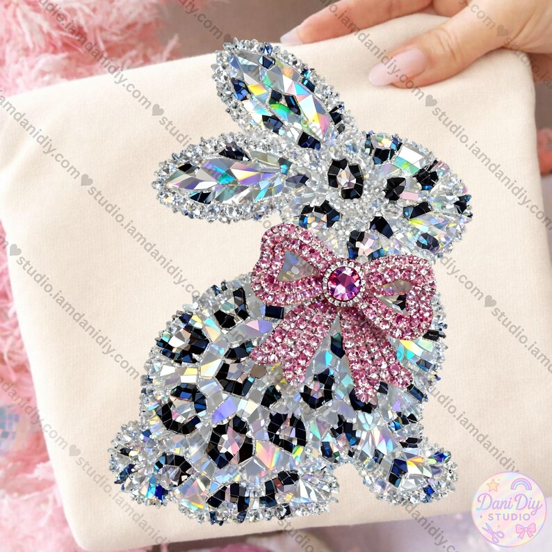 May include: A decorative bunny design with a leopard print pattern, embellished with sparkling crystals. The bunny features a pink bow with a central jewel. The design is set against a cream-colored background.