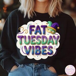 Puede incluir: Sudadera negra con el texto "FAT TUESDAY VIBES" en un diseño colorido y texturizado. El diseño incluye una máscara y un sombrero de Mardi Gras, con un borde blanco similar al encaje y cuentas decorativas. Prenda festiva.