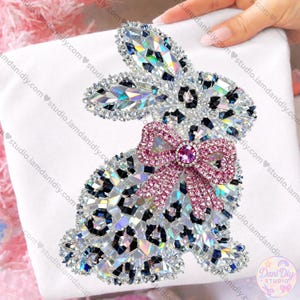 May include: A bedazzled bunny design with a pink bow and a leopard print pattern. The bunny is made of iridescent rhinestones and is set against a white background. The design is from Dani Diy Studio.