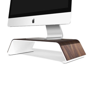 Può includere: Un supporto per monitor in legno di noce e bianco con un design curvo. Il supporto è progettato per sollevare un monitor per computer e creare uno spazio di lavoro più ergonomico.