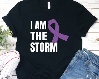 May include: Black t-shirt with white text that reads "I am the storm" and a purple ribbon.