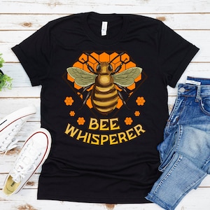 May include: Black t-shirt with a bee graphic and the text "BEE WHISPERER" in orange and white lettering.