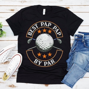 May include: Black t-shirt with a white golf ball and two golf clubs in the center of a circle. The circle has the text "Best Pap Pap By Par" with three stars above and below the golf ball.