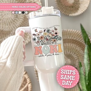 May include: A white stainless steel tumbler with a handle and clear lid, featuring a floral graphic, the text "LOVE THEM, RAISE THEM KIND, WATCH THEM GROW", the name "NONI" in large retro letters, and the names "isabella", "james", and "olivia" below.