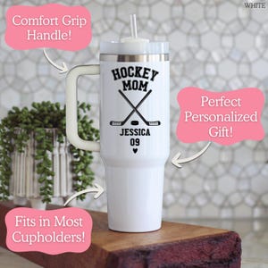 May include: A white stainless steel tumbler with a handle, a clear lid, and a straw. The front features black text reading HOCKEY MOM, JESSICA, and 09, along with a graphic of two crossed hockey sticks, a hockey puck, and a small heart symbol.