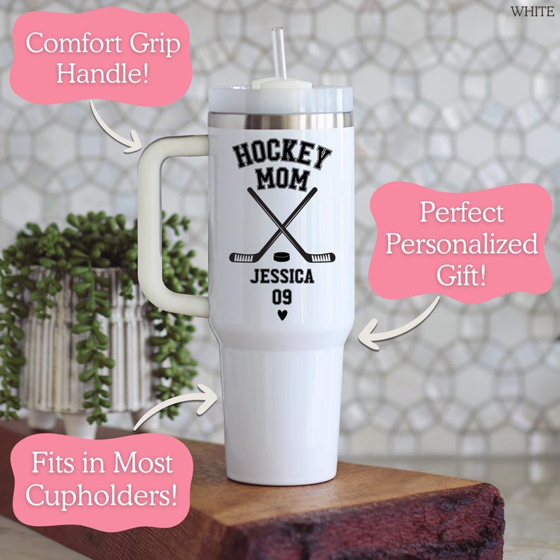 May include: A white stainless steel tumbler with a handle, a clear lid, and a straw. The front features black text reading HOCKEY MOM, JESSICA, and 09, along with a graphic of two crossed hockey sticks, a hockey puck, and a small heart symbol.