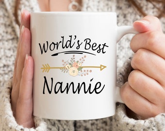 Può includere: Tazza in ceramica bianca con un design nero e oro. La tazza recita "World's Best Nannie" con un design floreale e una freccia.
