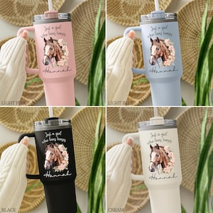 K&ouml;nnte beinhalten: Vier isolierte Becher mit Henkel und Trinkhalm in den Farben Hellrosa, Hellblau, Schwarz und Creme. Jeder Becher zeigt eine Pferdeillustration, rosa Blumenakzente sowie den Schriftzug "Just a girl who loves horses" und den Namen "Hannah".