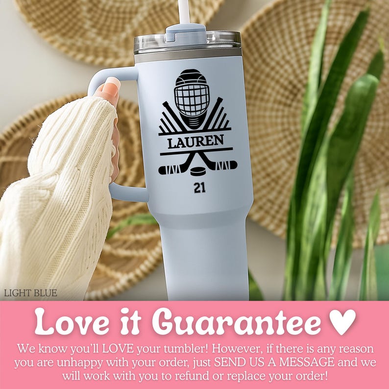 May include: A pale blue tumbler featuring a black hockey design with a helmet, crossed sticks, and a puck. The name "LAUREN" and the number "21" are printed on the tumbler. It has a handle and a straw.