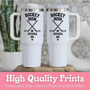 May include: Two white stainless steel tumblers with handles and clear lids. Each features black text reading HOCKEY MOM, JESSICA, and 09, with a graphic of two crossed hockey sticks, a puck, and a small heart printed on the front surface.