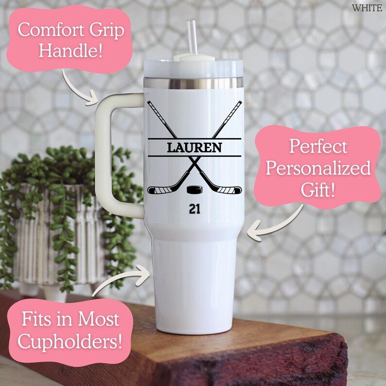 May include: White insulated travel mug with a comfort grip handle and a straw. The mug has a hockey design with the name "LAUREN" and the number "21".